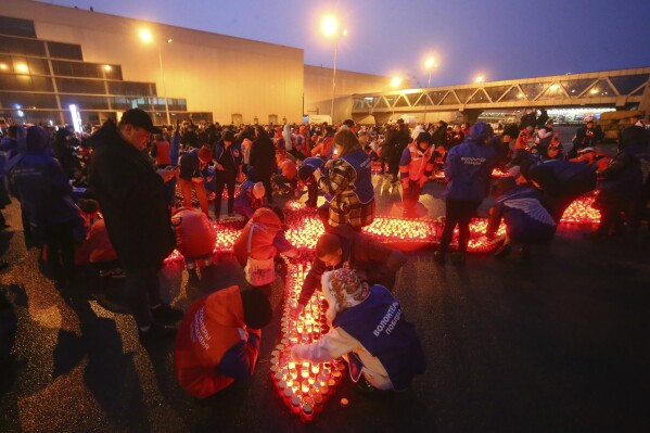 People light candles and lay flowers at a makeshift memorial in front of the Crocus City Hall on the western outskirts of Moscow, Russia, on Sunday, March 24, 2024. There were calls Monday for harsh punishment for those behind the attack on the Russia concert hall that killed more than 130 people as authorities combed the burnt-out ruins of the shopping and entertainment complex in search of more bodies. (Sergei Vedyashkin, Moscow News Agency via AP)