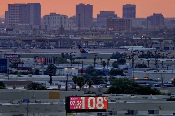 FILE - A sign displays an unofficial temperature as jets taxi at Sky Harbor International Airport at dusk, July 12, 2023, in Phoenix. (AP Photo/Matt York, File)