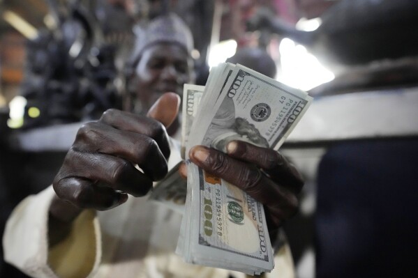 A man counts U.S. $100 bills at the craft and art market in Lagos, Nigeria, on Wednesday, Aug. 16, 2023. Across the developing world, many countries are fed up with America's dominance of the global financial system — and especially the power of the dollar. (AP Photo/Sunday Alamba)