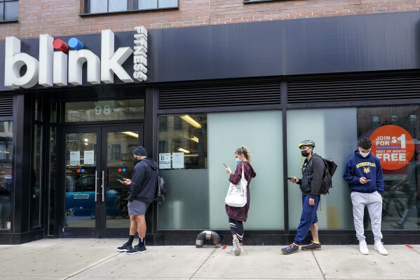 FILE — People line up outside the Blink Fitness gym, March 26, 2021, in the Lower East Side neighborhood of New York. (AP Photo/Mary Altaffer, File)