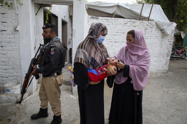 ARCHIVO - Un agente de policía mira mientras una trabajadora de salud, a la derecha, administra una vacuna contra la polio a un niño en un vecindario de Peshawar, Pakistán, el 9 de septiembre de 2024. (AP Foto/Muhammad Sajjad, Archivo)