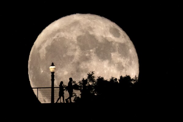 People walk in front of a rising supermoon at Griffith Observatory in Los Angeles, Monday, Aug. 19, 2024. (AP Photo/Richard Vogel)