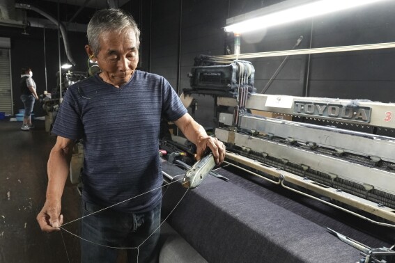 Shigeru Uchida, a weaver at Momotaro Jeans, holds a wooden shuttle next to a vintage loom machine in Kojima, Okayama prefecture, Japan, on Sept. 4, 2024. (AP Photo/Ayaka McGill)