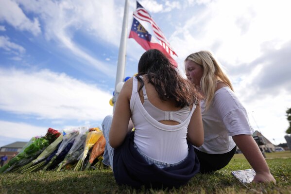 Two students view a memorial as the flags fly half-staff after a shooting Wednesday at Apalachee High School, Thursday, Sept. 5, 2024, in Winder, Ga. (AP Photo/Mike Stewart)