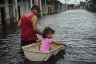 Jesús Hernández con su nieta Angelina en una calle inundada tras el paso del huracán Helene en Batabano, provincia de Mayabeque, Cuba, el 26 de septiembre del 2024. (Foto AP /Ramon Espinosa)