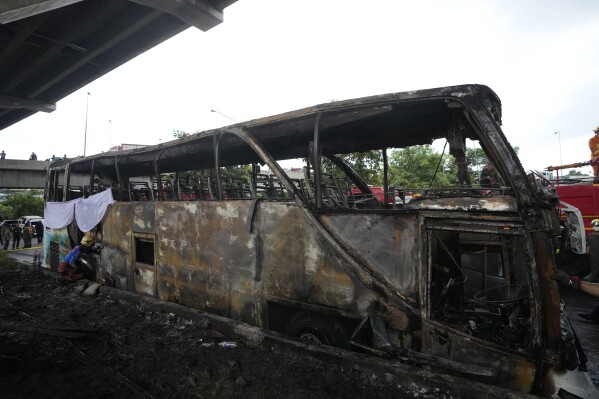 FILE - A rescuer inspects a bus that caught fire, carrying young students with their teachers, in suburban Bangkok, Tuesday, Oct. 1, 2024. (AP Photo/Sakchai Lalit, File)