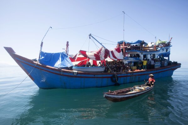 Un pescador local pasa junto a un barco con refugiados rohinya anclado en aguas cerca de la costa de Labuhan Haji, en la provincia de Aceh, Indonesia, el martes 22 de octubre de 2024. (AP Foto/Binsar Bakkara)