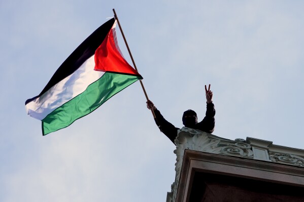 A student protester waves a Palestinian flag above Hamilton Hall on the campus of Columbia University, Tuesday, April 30, 2024, in New York. Early Tuesday, dozens of protesters took over Hamilton Hall, locking arms and carrying furniture and metal barricades to the building. Columbia responded by restricting access to campus. (Pool Photo/Mary Altaffer)