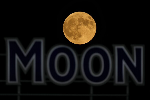 The full moon rises in the over a beer sign in the outfield at Kauffman Stadium during a baseball game between the Kansas City Royals and the Detroit Tigers, Tuesday, Sept. 17, 2024, in Kansas City, Mo. (AP Photo/Charlie Riedel)