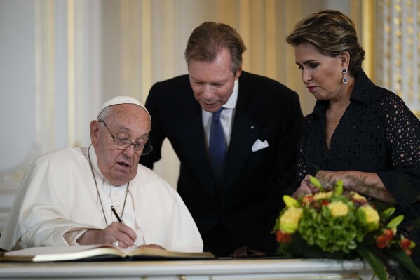 El papa Francisco, flanqueado por el gran duque de Luxemburgo, Enrique, y la gran duquesa María Teresa, firma el libro de visitas el jueves 26 de septiembre de 2024, en el Gran Palacio Ducal de Luxemburgo. (AP Foto/Andrew Medichini)