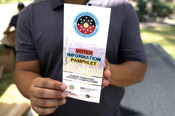 Alexander Castillo-Nunez, a civic engagement coordinator at the Inter Tribal Council of Arizona, Inc., shows a voter information pamphlet at an Arizona Native Vote booth during an Indigenous Peoples' Day event, Monday, Oct. 14, 2024, in Phoenix. (AP Photo/Ross D. Franklin)