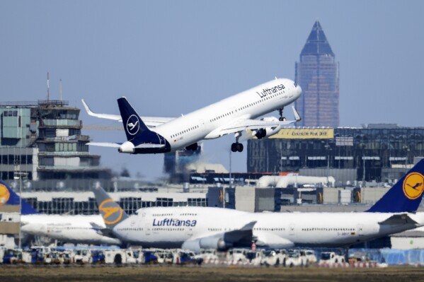 FILE - A Lufthansa Airbus takes off at Frankfurt Airport above other passenger aircraft of the airline, Germany, Monday, March 23, 2020. (Arne Dedert/dpa via AP, File)