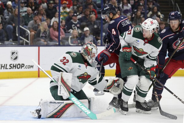 Minnesota Wild goalie Filip Gustavsson (32) makes a stop in front of Columbus Blue Jackets forward Cole Sillinger (4), forward Mathieu Olivier (24) and Wild defenseman Declan Chisholm (47) during the second period of an NHL hockey game in Columbus, Ohio, Saturday, Oct. 19, 2024. (AP Photo/Paul Vernon)