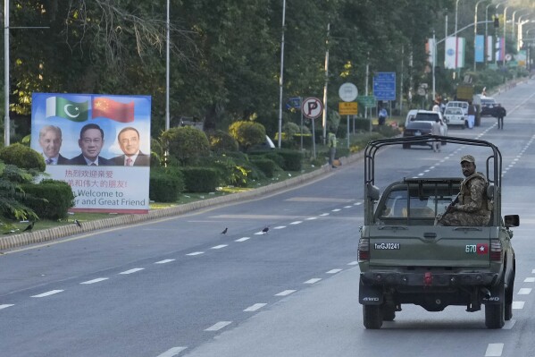 An army vehicle moves past a welcoming billboard with portraits of China's Premier Li Qiang, center, Pakistan's Prime Minister Shehbaz Sharif and President Asif Ali Zardari, displayed along a road leading to the venue of the upcoming Shanghai Cooperation Organization (SCO) summit in Islamabad, Pakistan, Sunday, Oct. 13, 2024. (AP Photo/Anjum Naveed)