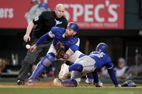 Texas Rangers catcher Carson Kelly reaches out for the throw before tagging out Toronto Blue Jays' Ernie Clement, right, who was trying to score on a Vladimir Guerrero Jr. single as umpire Mike Estabrook, rear, looks on in the fourth inning of a baseball game in Arlington, Texas, Thursday, Sept. 19, 2024. (AP Photo/Tony Gutierrez)