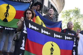 FILE - Demonstrators hold Kanak and Socialist National Liberation Front (FLNKS) flags during a gathering in Paris, Thursday May.16, 2024. A pro-independence movement in the French Pacific territory of New Caledonia is demanding the “release and immediate return” of the Indigenous Kanak leader who was flown more than 10,000 miles to mainland France for pretrial detention. Christian Tein, a leader of the movement known as The Field Action Coordination Unit, and six other Kanak activists are now awaiting trial over their alleged role in recent deadly unrest. (AP Photo/Thomas Padilla, File)