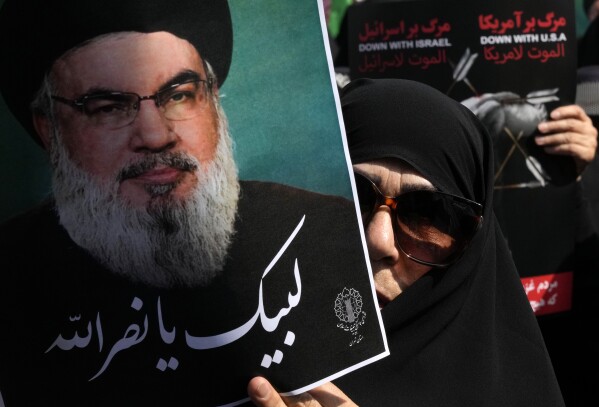 An Iranian worshipper holds up a poster of Hezbollah leader Sayyed Hassan Nasrallah, reading in Arabic: "At your service Nasrallah" during an anti-Israeli rally after Friday prayers in Tehran, Iran, Friday, Sept. 27, 2024. (AP Photo/Vahid Salemi)