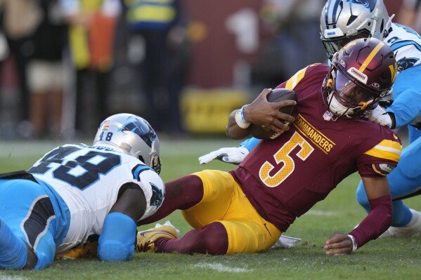 Washington Commanders quarterback Jayden Daniels (5) is tackled by Carolina Panthers linebacker Thomas Incoom (48) during the first half of an NFL football game, Sunday, Oct. 20, 2024, in Landover, Md. (AP Photo/Stephanie Scarbrough)