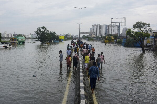 People walk by the median of a flooded road following heavy rains along the Bay of Bengal coast in Chennai, India, Tuesday, Dec.5, 2023. Tropical Storm Michaung began making landfall along India's southeastern coastline Tuesday, bringing with it torrential rains and strong winds. (AP Photo)