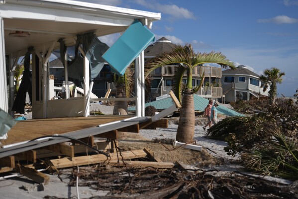 FILE - Resident Kerry Flynn, right, and a friend walk past a damaged home and the displaced roof of their 55+ mobile home community's tiki hut after the passage of Hurricane Milton, on Manasota Key, in Englewood, Fla., Oct. 13, 2024. (AP Photo/Rebecca Blackwell, File)