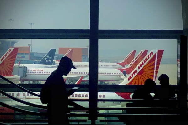 FILE - A man is silhouetted against an airport window with Air India aircrafts parked in the background in New Delhi, India, Oct. 31, 2023. (AP Photo/Manish Swarup, File)