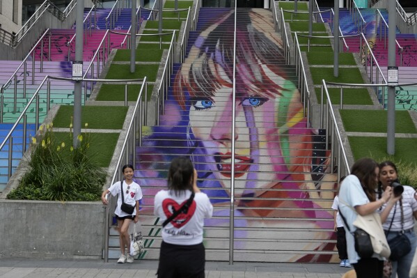 Fans pose by a Taylor Swift portrait painted on a stairway at Wembley Stadium in London, Wednesday, Aug. 14, 2024, ahead of a series of Taylor Swift concerts starting Thursday. (AP Photo/Alastair Grant)