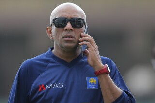 FILE - Sri Lanka's coach Chandika Hathurusinghe speaks from a mobile phone before a practice session ahead of the first test cricket match against South Africa in Galle, Sri Lanka, Wednesday, July 11, 2018. (AP Photo/Eranga Jayawardena, File)