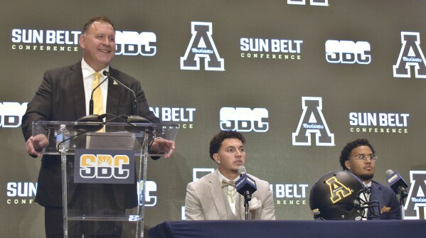 Appalachian State head coach Shawn Clark speaks while quarterback Joey Agulilar, center and wide receiver Kaedin Robinson, right, listen at the Sun Belt Conference NCAA college football media days in New Orleans Tuesday, July 23, 2024. (Aimee Cronan/The Gazebo Gazette via AP)