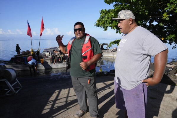 Fishermen Taula Fagatuai, left, and Faalogo Afereti Taliulu talk on Tuesday, Oct. 22, 2024, about the New Zealand navy ship HMNZS Manawanui that sank not far from them in the village of Siumu, Samoa. (AP Photo/Rick Rycroft)