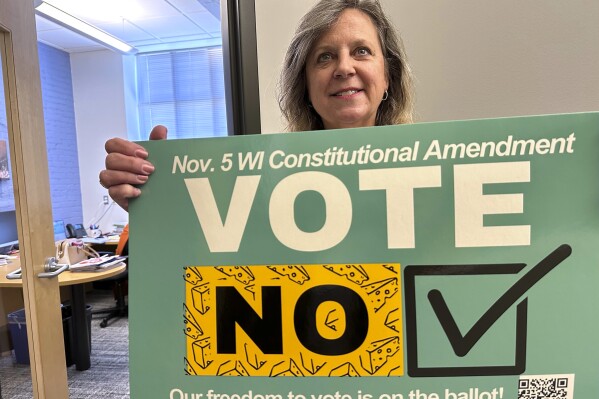 Debra Cronmiller, executive director of the League of Women Voters of Wisconsin, holds a sign outside her Madison office, Wednesday, Oct. 16, 2024, urging voters on Nov. 5 to reject a Republican-authored amendment to the state constitution that would explicitly prohibit foreign nationals from voting in Wisconsin. (AP Photo/Todd Richmond)