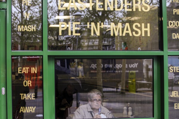 FILE - A woman sits at an pie eatery in East London, May, 14, 2012. (AP Photo/Lefteris Pitarakis, File)