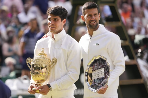 Carlos Alcaraz of Spain holds his trophy as he stands with Novak Djokovic of Serbia after winning the men's singles final at the Wimbledon tennis championships in London, Sunday, July 14, 2024. (AP Photo/Alberto Pezzali)