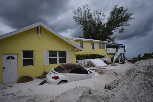 A car sits half-buried in sand as Bradenton Beach, Fla., which was in the process of cleaning up after Hurricane Helene, as Hurricane Milton approaches on Anna Maria Island, Tuesday, Oct. 8, 2024. (AP Photo/Rebecca Blackwell)