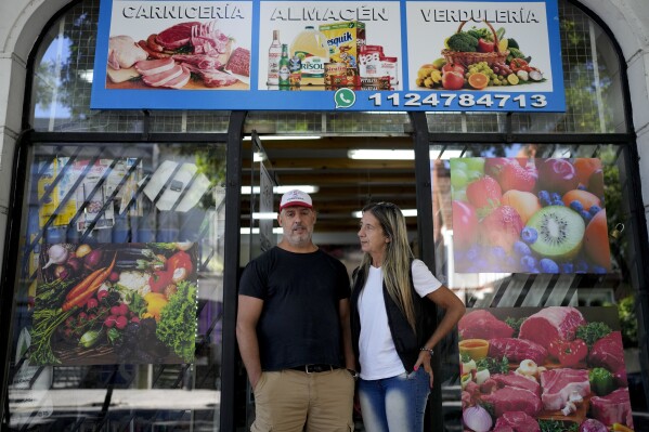 Sergio Gómez and Carla Cavallini pose for a picture outside their store, in Buenos Aires, Argentina, Wednesday, March 6, 2024. Gómez and his wife are among a large group of Argentines who say their economic situation is worse now than a year ago as a consequence of a series of austerity and deregulation measures ordered by President Javier Milei in his first 100 days in office. (AP Photo/Natacha Pisarenko)