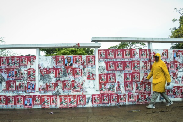 A pedestrian passes a wall of election posters in Maputo, Sunday, Oct. 6, 2024, ahead of elections to be held in Mozambique. (AP Photo/Carlos Uqueio)