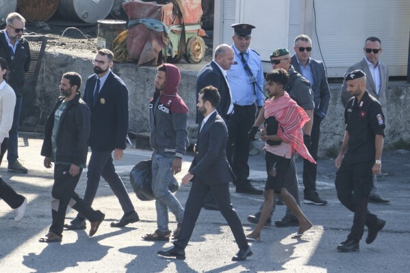 FILE - Migrant and security officials walk at the port of Shengjin, northwestern Albania. Wednesday, Oct. 16, 2024 after disembarking from the Italian navy ship Libra, carrying the first group of 16 migrants intercepted in international waters. (AP Photo/Vlasov Sulaj, File)