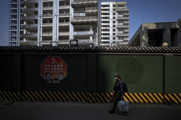 FILE - A woman carrying her belonging walks by a luxury housing construction site in Beijing, Tuesday, Sept. 24, 2024. (AP Photo/Andy Wong, File)